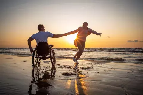 personne handicapé qui tient la main de son compagnon sur la plage au soleil couchant