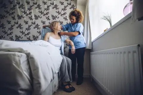 femme qui aide une sénior à se lever du lit 